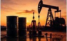 An oil pump jack and barrels at sunset